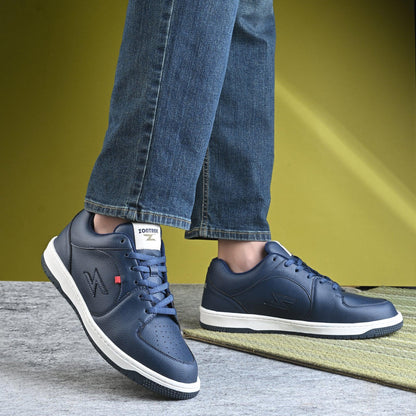 Navy blue sneakers with white soles worn with blue jeans on a green and gray surface.