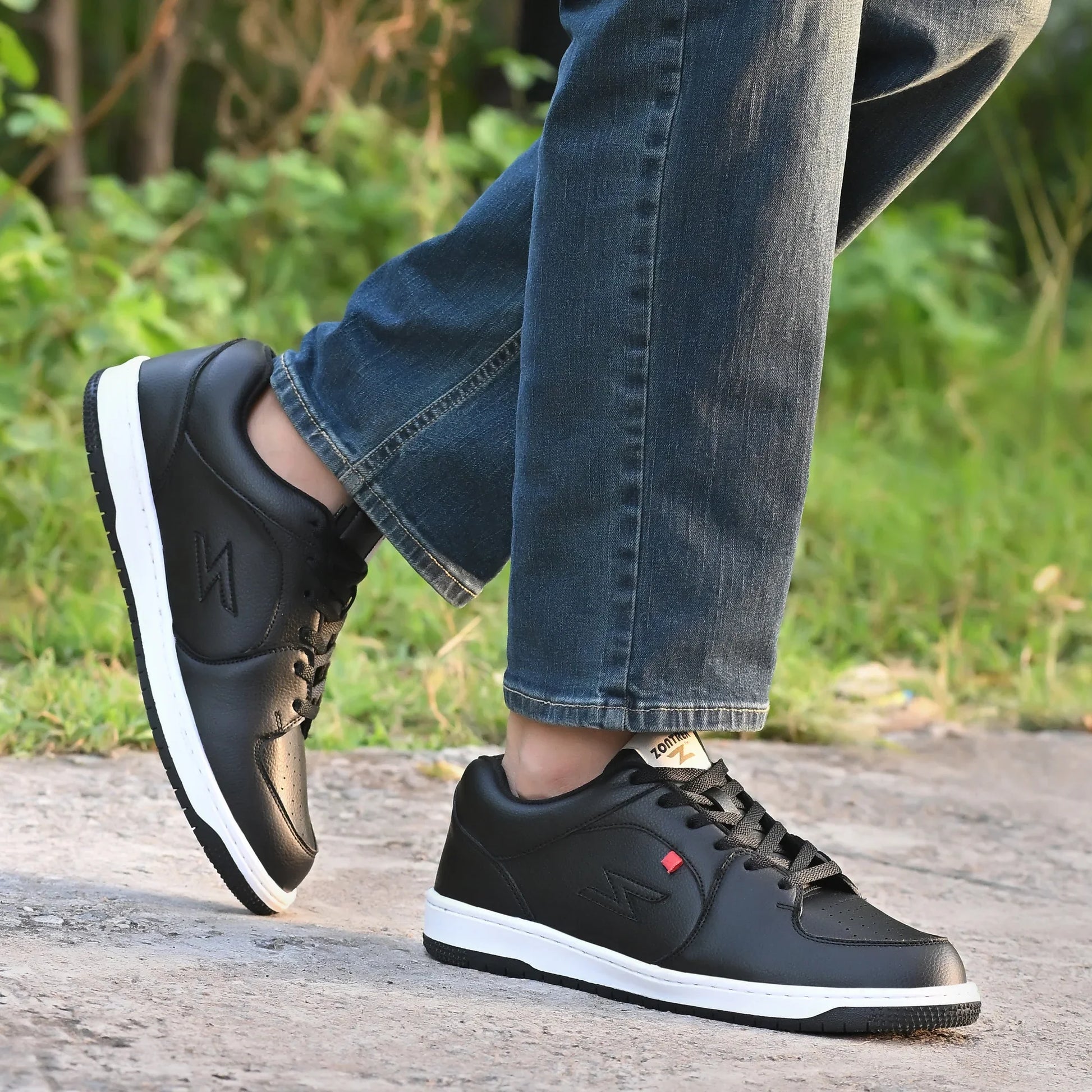 Black sneakers with white soles worn with blue jeans on a natural background